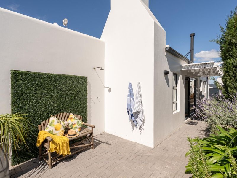 A well-maintained paved patio area featuring an outdoor shower, a chimney stack, and a pergola, providing a pleasant outdoor space.