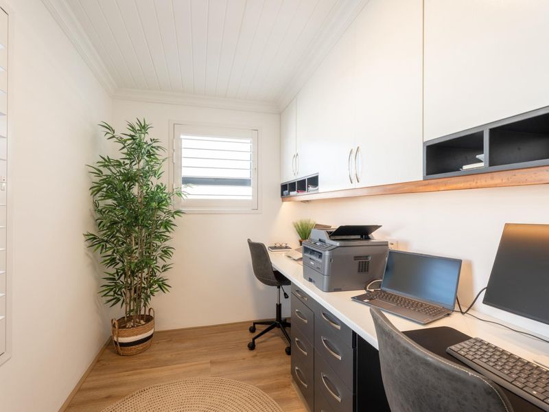 A well-appointed home office featuring custom built-in cabinetry, integrated desk space, modern laminate flooring, and bright, clean finishes.