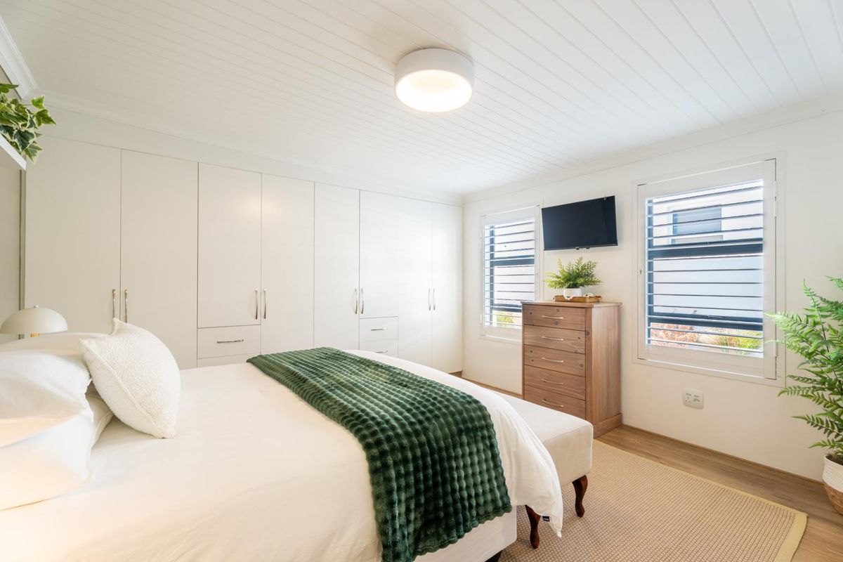 A bright and well-maintained bedroom featuring extensive built-in cabinetry, tongue and groove ceiling detail, and functional louvre shutters for light control.