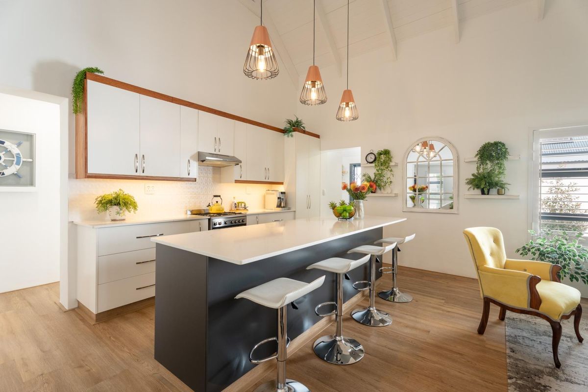 Modern kitchen featuring a central island with breakfast bar, sleek white cabinetry, quartz countertops, and high vaulted ceilings with pendant lighting.