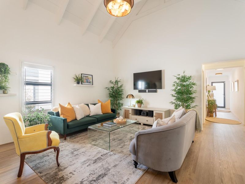 Bright and airy living room featuring a high vaulted ceiling with exposed rafters, laminate flooring, and large windows with shutter blinds.