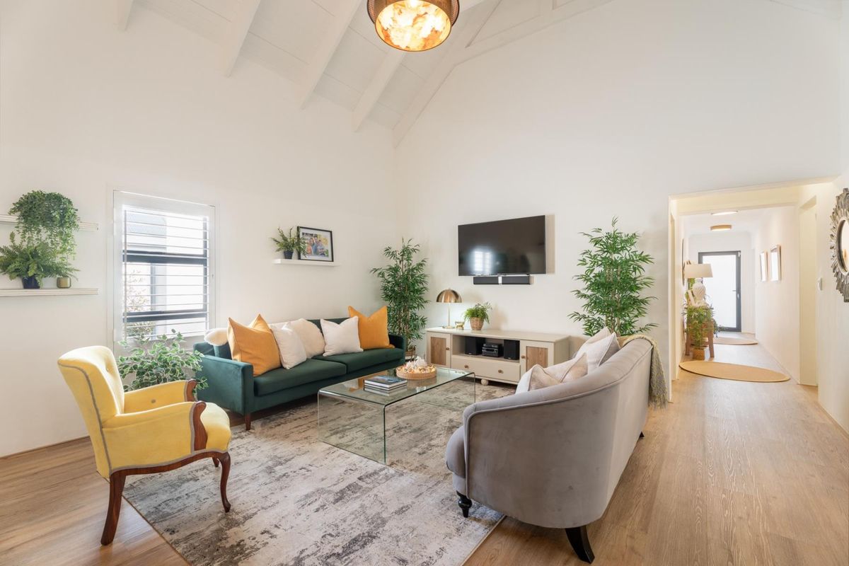Bright and airy living room featuring a high vaulted ceiling with exposed rafters, laminate flooring, and large windows with shutter blinds.