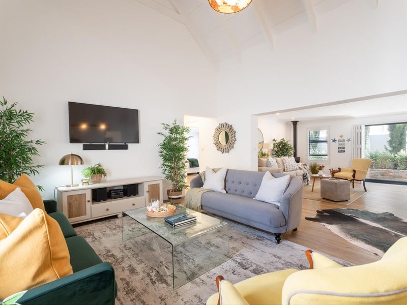 Spacious open-plan living area featuring a high vaulted ceiling with exposed rafters, wood-burning stove, and seamless flow to the outdoor patio through sliding doors.