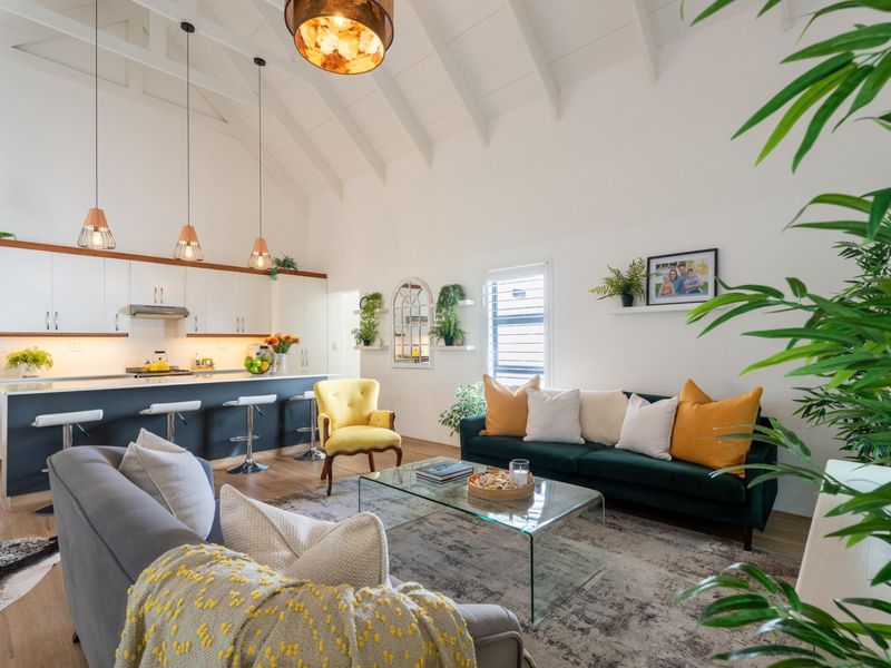 Spacious open-plan living area featuring a vaulted ceiling with exposed rafters, modern kitchen with island, and high-quality finishes throughout.