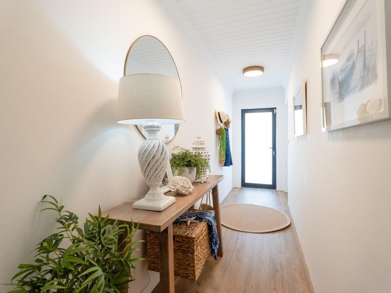 A bright and well-maintained hallway featuring timber-look flooring, a tongue and groove ceiling, and a modern glass-panelled external door.