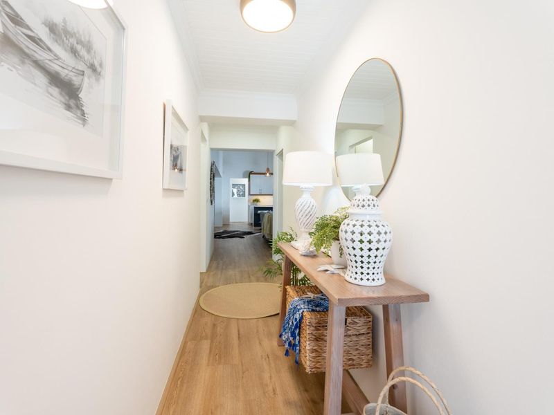 A bright and well-maintained hallway featuring timber-look flooring and a classic beadboard ceiling, leading through to the main living area.