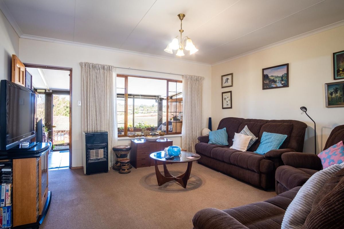 A comfortable living room featuring carpeted flooring, timber-framed windows, and access to an adjoining patio area.