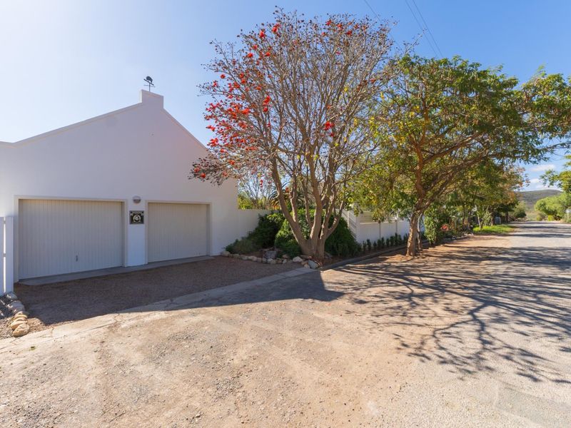 Street-facing view of a property featuring a double garage, white perimeter fencing, and a gravel driveway with mature trees.