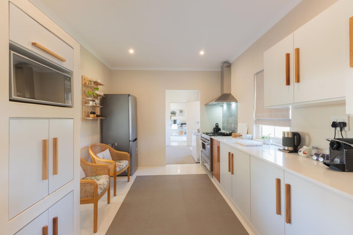 A modern, well-maintained kitchen featuring white cabinetry with wooden handles, stone countertops, built-in appliances, and recessed lighting.