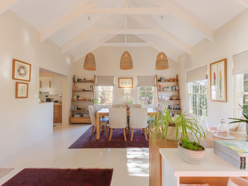 Bright open-plan living and dining area featuring a high vaulted ceiling with exposed rafters, large sash windows, and integrated shelving.