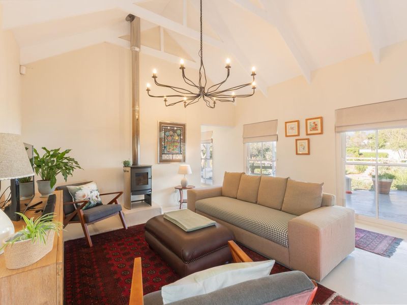 A bright living room featuring a vaulted ceiling with exposed rafters, a modern freestanding wood-burning fireplace, and large sliding glass doors leading outdoors.
