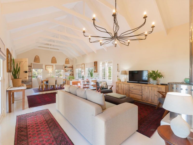 Spacious open-plan living and dining area featuring a high vaulted ceiling with exposed rafters, a feature chandelier, and a modern freestanding fireplace.