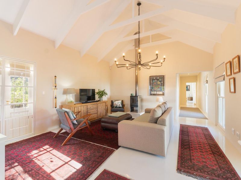 Spacious living room featuring a high vaulted ceiling with exposed rafters, a central freestanding fireplace, and direct access to the garden through french doors.