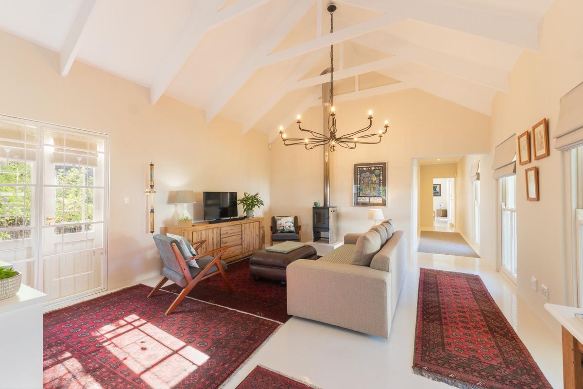Spacious living room featuring a high vaulted ceiling with exposed rafters, a central freestanding fireplace, and direct access to the garden through french doors.