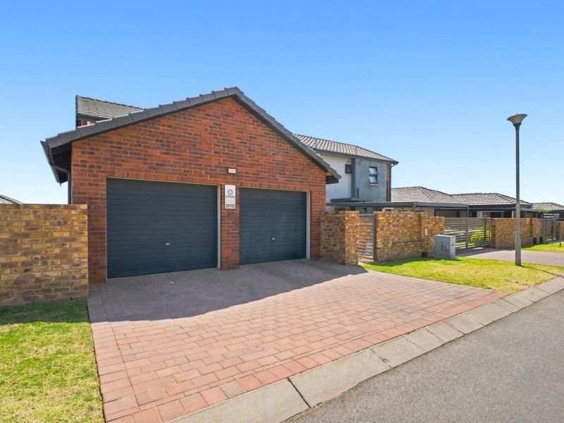 Front exterior view of a townhouse featuring a double garage, paved driveway, and brick boundary wall with a pedestrian gate.