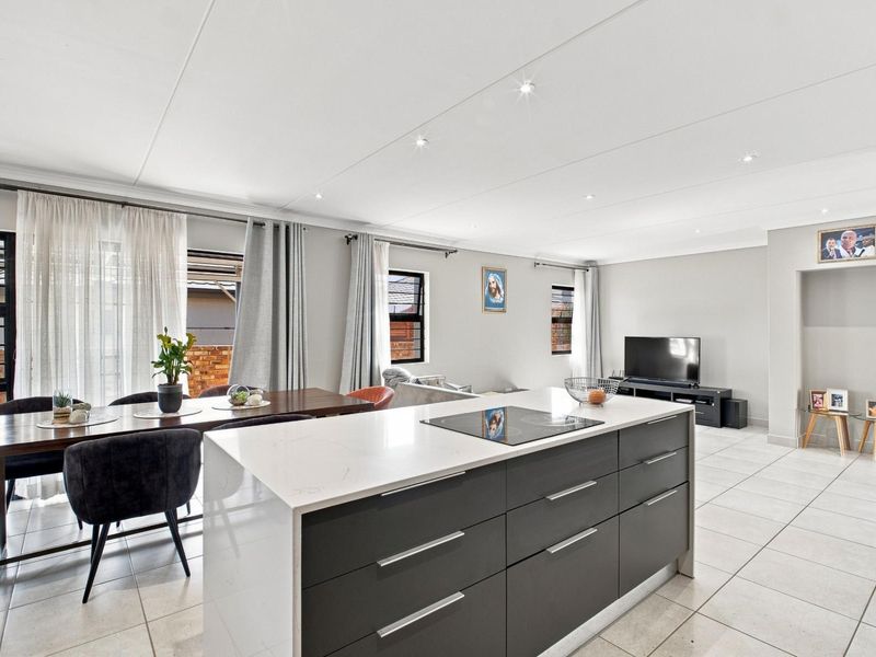 Modern open-plan living area featuring a central kitchen island with a built-in hob, tiled flooring, and recessed ceiling lighting, creating a bright, functional space.