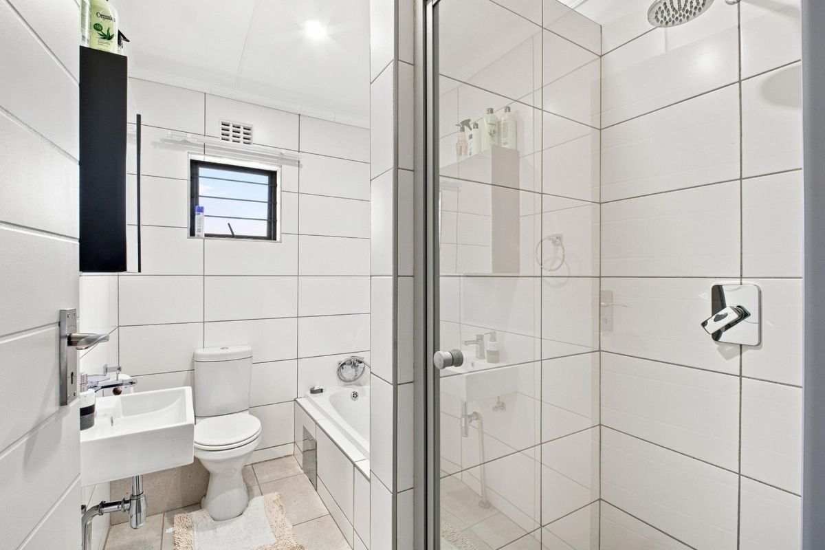 A modern, clean bathroom featuring a wall-mounted basin, toilet, built-in bathtub, and a separate glass-enclosed shower with white tiled finishes.