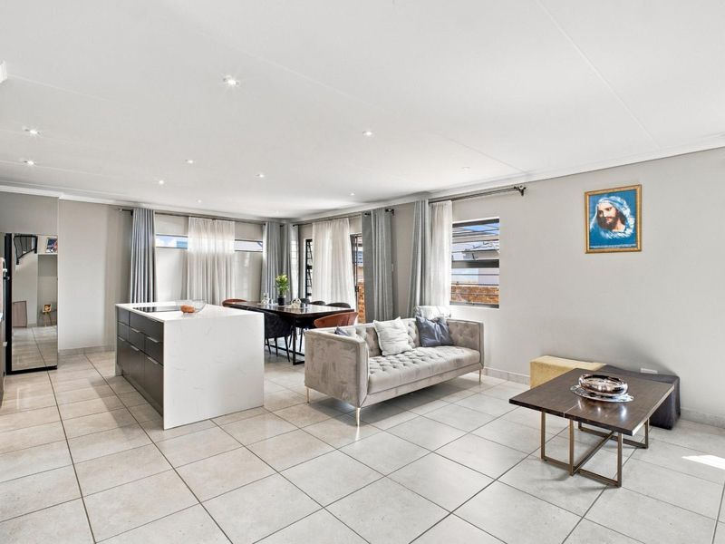 Spacious open-plan living and kitchen area featuring a modern kitchen island, neutral tiled flooring, and recessed lighting throughout.