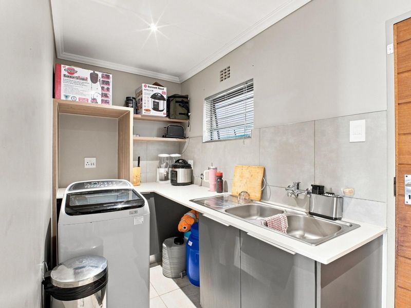 A functional laundry room featuring a double stainless steel sink, tiled splashback, built-in cabinetry, and a dedicated space for a washing machine.