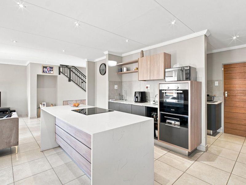 Modern open-plan kitchen featuring a central island with induction hob, built-in oven, and contemporary cabinetry, seamlessly flowing into the living area.