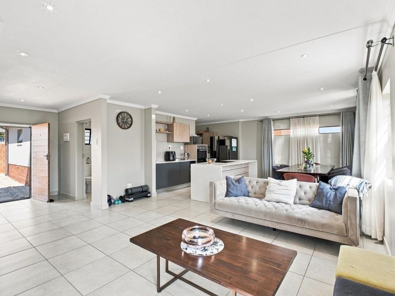 Spacious open-plan living area featuring a modern kitchen with a central island, tiled floors, and recessed lighting, seamlessly connecting to the dining and lounge space.