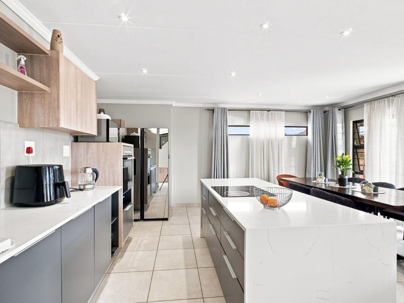 Modern open-plan kitchen featuring a large island with quartz countertops, integrated appliances, sleek cabinetry, and recessed lighting, seamlessly flowing into the dining area.