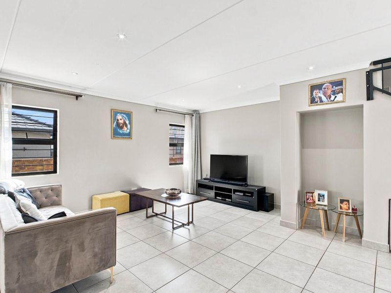 A bright and spacious living room featuring neutral tiled flooring, recessed downlighting, and a built-in staircase alcove.
