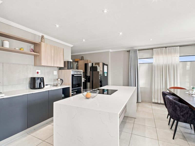Modern open-plan kitchen and dining area featuring a large central island with quartz countertops, sleek cabinetry, and integrated appliances.