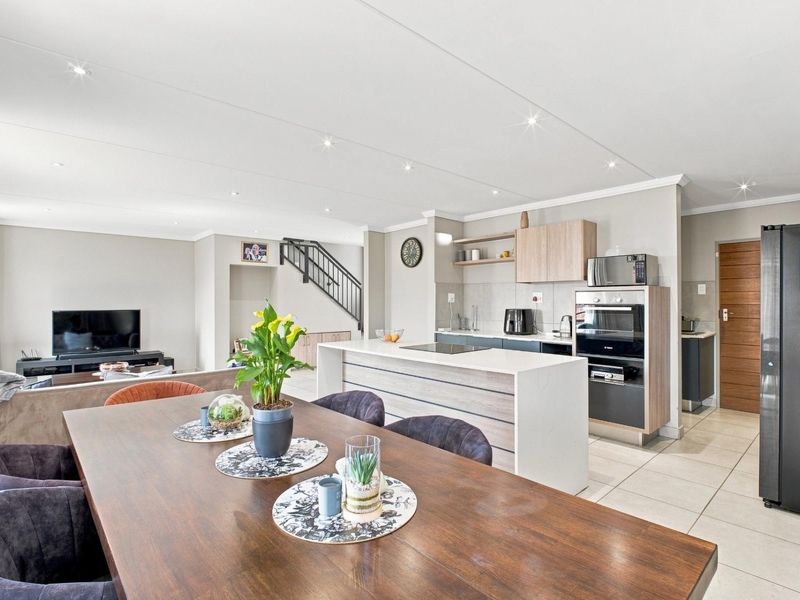 Modern open-plan living and dining area featuring a contemporary kitchen with a central island, built-in appliances, and tiled flooring throughout.