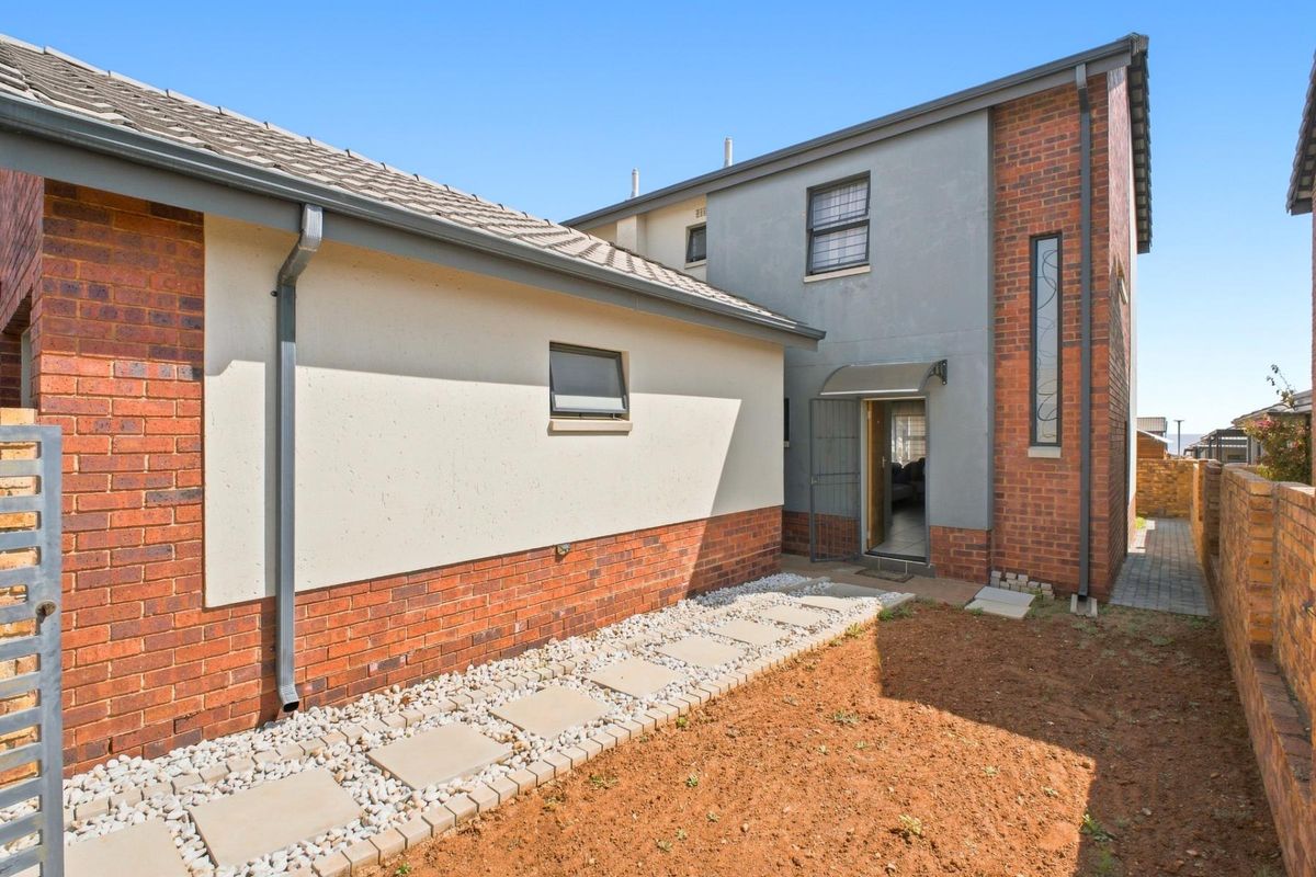 Rear exterior view of the townhouse featuring a brick and rendered facade, tiled roof, and a paved walkway leading to the entrance.