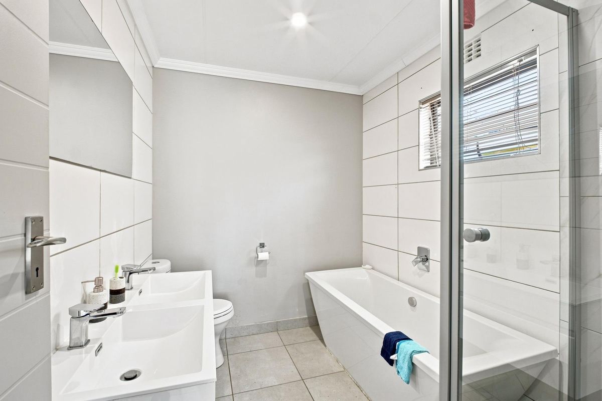 Modern bathroom featuring a double vanity, a built-in bathtub, and a separate glass-enclosed shower with neutral tiled finishes.