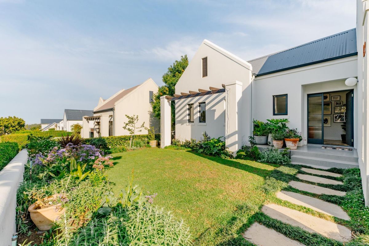 A well-maintained rear garden featuring a landscaped lawn, stone paver pathway, and a modern pergola attached to the white-walled residence.