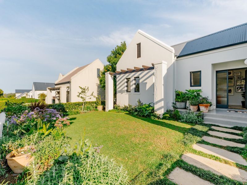 A well-maintained rear garden featuring a landscaped lawn, stone paver pathway, and a modern pergola attached to the white-walled residence.