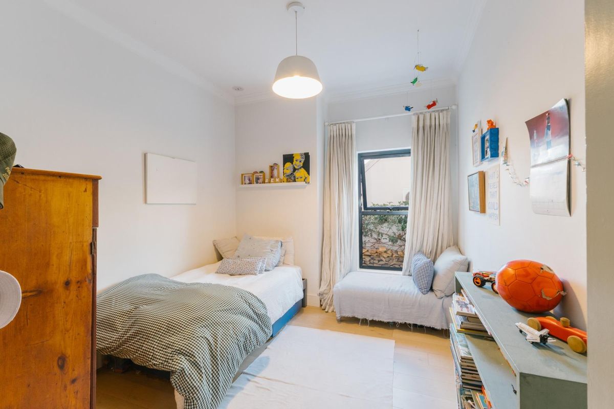 A bright and well-maintained bedroom featuring light wood flooring, coving, and a large window with natural light.