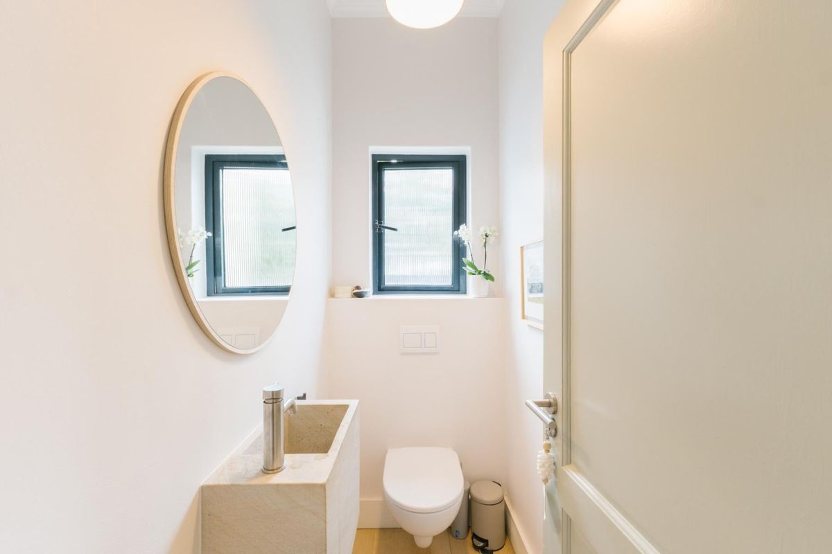 A modern, minimalist powder room featuring a unique stone basin, wall-hung toilet with concealed cistern, and clean, neutral finishes.