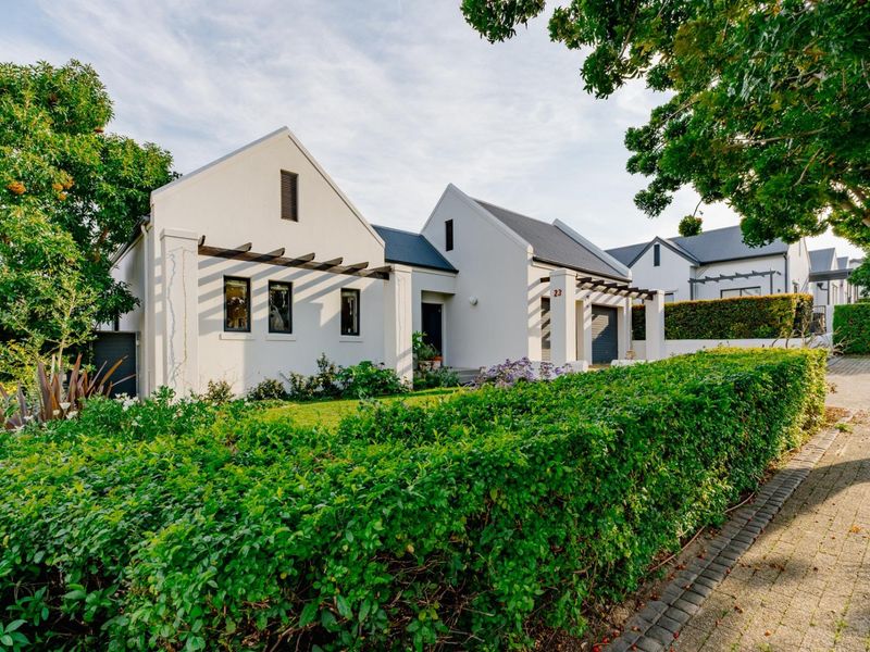 A well-maintained modern home featuring a gabled facade, pergola, and neatly landscaped garden with a paved driveway.