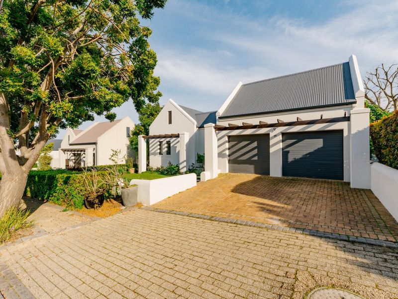 Front exterior view of a modern house featuring a double garage, paved driveway, and architectural pergola details.