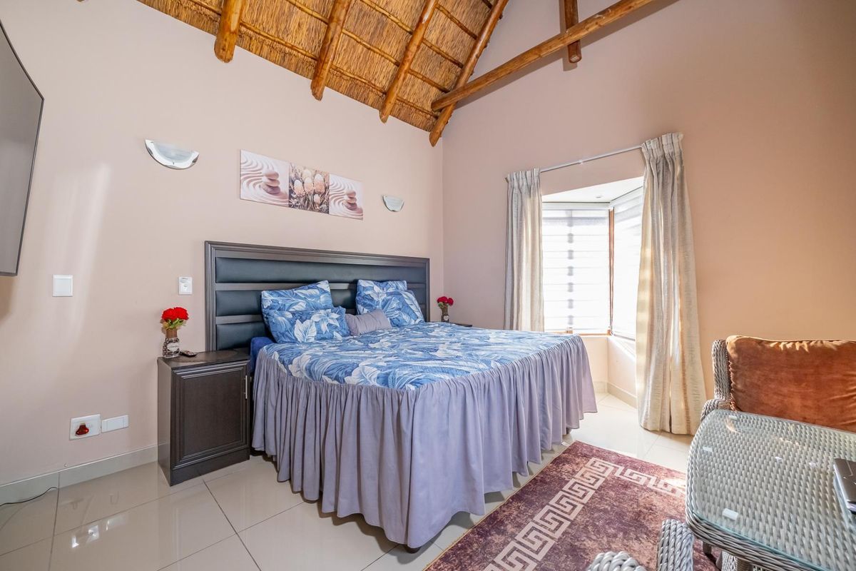 Spacious bedroom featuring a high vaulted thatched ceiling with exposed timber rafters, tiled flooring, and a bright bay window.