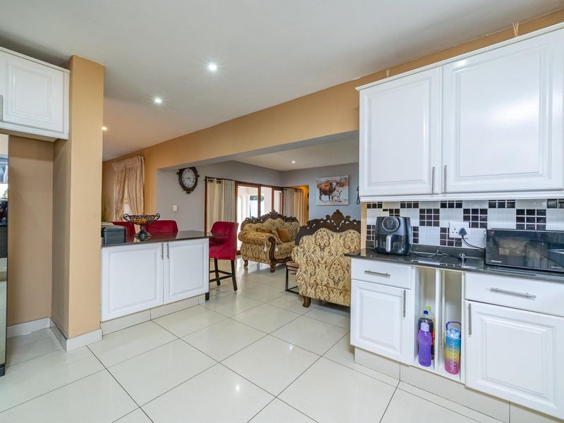 Open-plan kitchen and living area featuring white cabinetry, black granite countertops, and neutral porcelain floor tiles throughout the space.