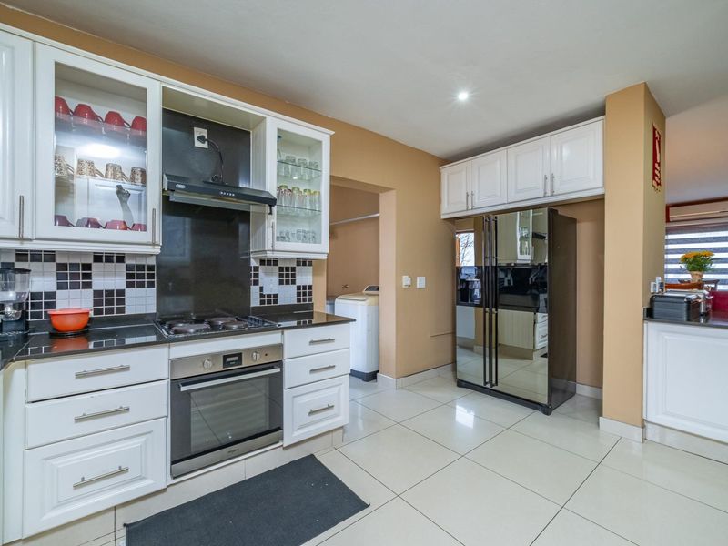 A well-maintained kitchen featuring white cabinetry, granite countertops, a built-in oven with gas hob, and a tiled backsplash, with an adjacent scullery area.