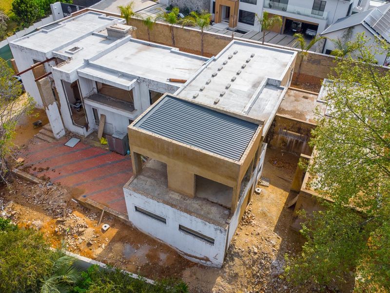 Aerial view of a residential property currently under construction, featuring a flat roof design, paved patio area, and unfinished exterior surfaces.