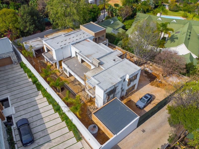 Aerial view of a residential property currently under construction, featuring a flat-roof structure, concrete driveway, and unlandscaped grounds.