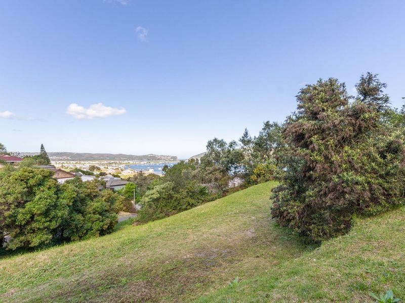 A scenic view overlooking the coastal landscape and residential area from a sloped, grass-covered vacant plot.