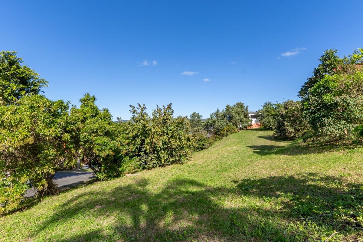 A sloped residential plot featuring established trees and a grass lawn, offering a natural setting for potential development.
