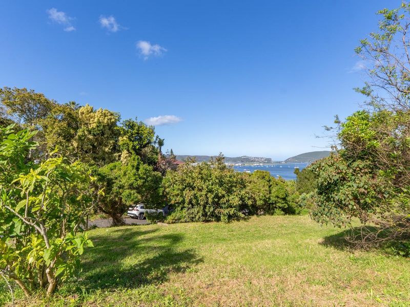 A scenic view of the coastal landscape and water, framed by established trees and greenery on the residential land.