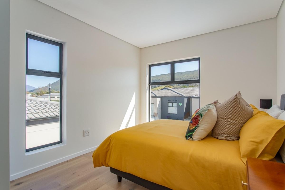 A bright, modern bedroom featuring laminate flooring and large aluminium-framed windows with views of the surrounding estate.