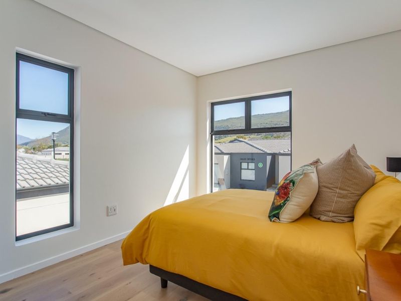 A bright, modern bedroom featuring laminate flooring and large aluminium-framed windows with views of the surrounding estate.