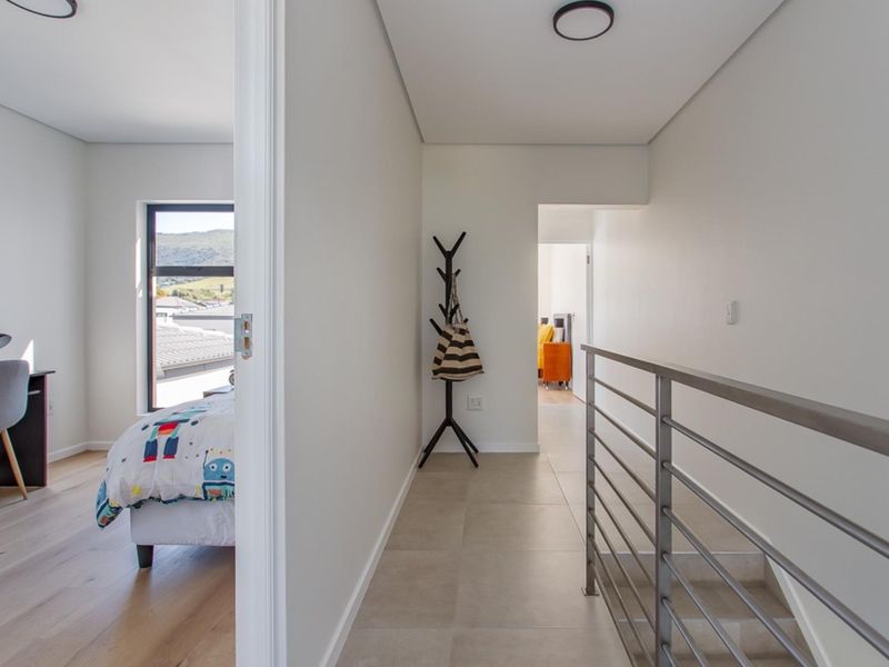 A bright, modern hallway featuring tiled flooring and a sleek metal balustrade, providing access to adjacent bedrooms.