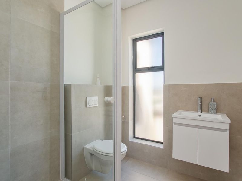 Modern bathroom featuring a wall-mounted toilet, vanity cabinet with basin, and a shower enclosure with neutral wall tiling.