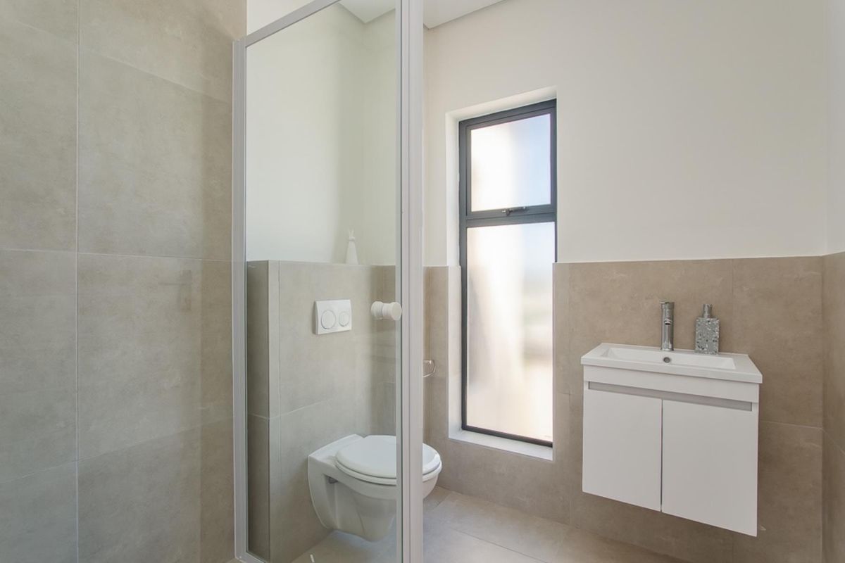 Modern bathroom featuring a wall-mounted toilet, vanity cabinet with basin, and a shower enclosure with neutral wall tiling.
